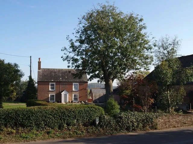 Hicks Farm on Throop Road, with the listed farmhouse set back behind the hedge and farm buildings on the right. The picture does not show the site as it is today