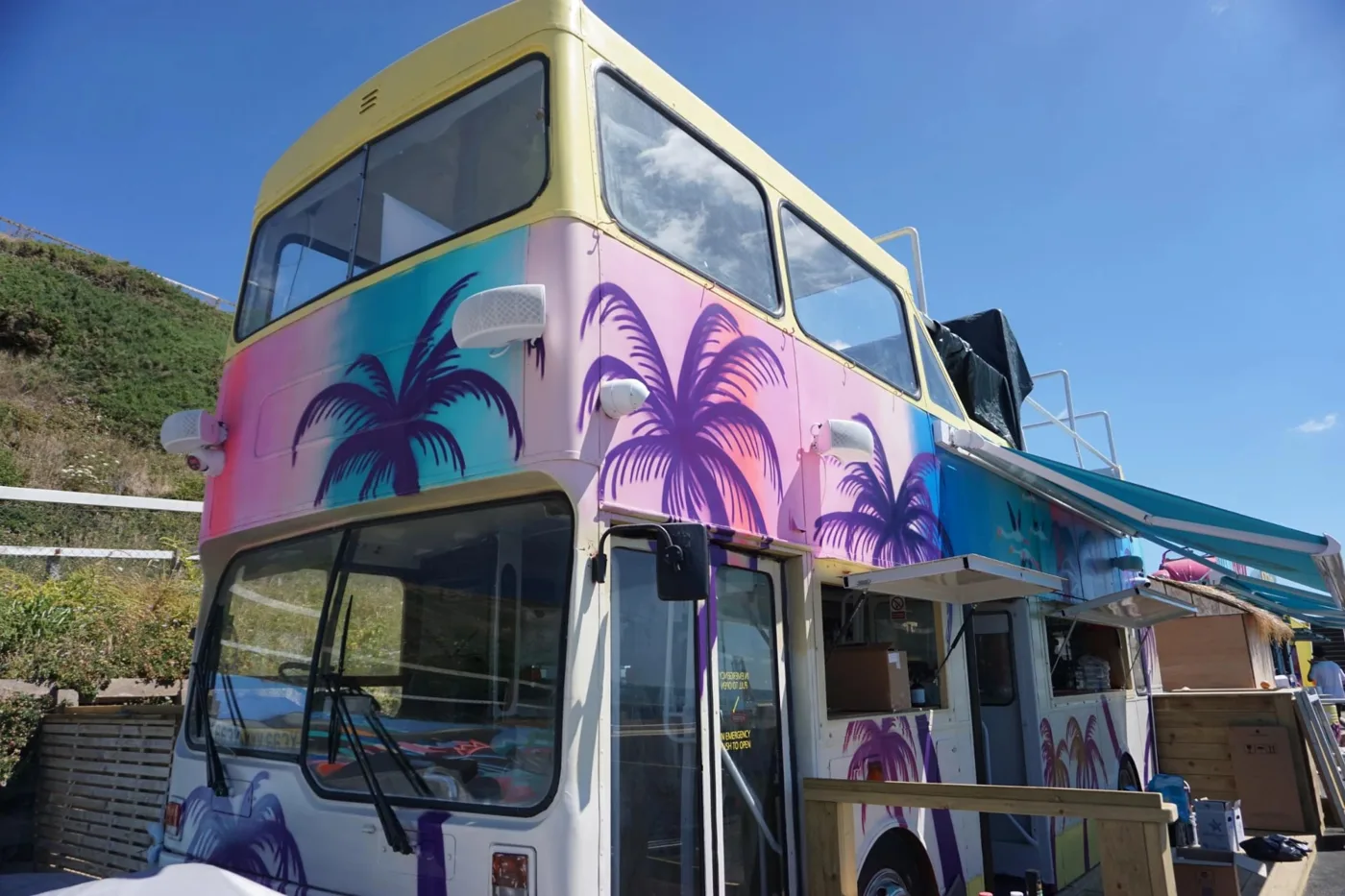 A double-decker bus painted with purple palm trees, used as a bar at SOBO Beach